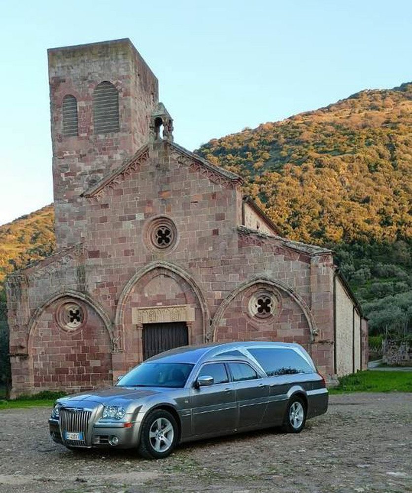Carro funebre grigio dell'Agenzia Funebre Pinna davanti alla chiesa romanica di San Pietro a Bosa