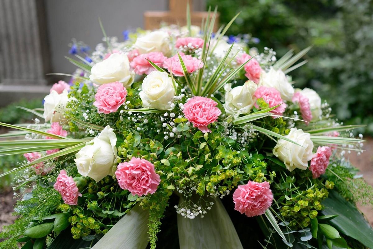 Composizione funebre di rose bianche e garofani rosa con nastro chiaro